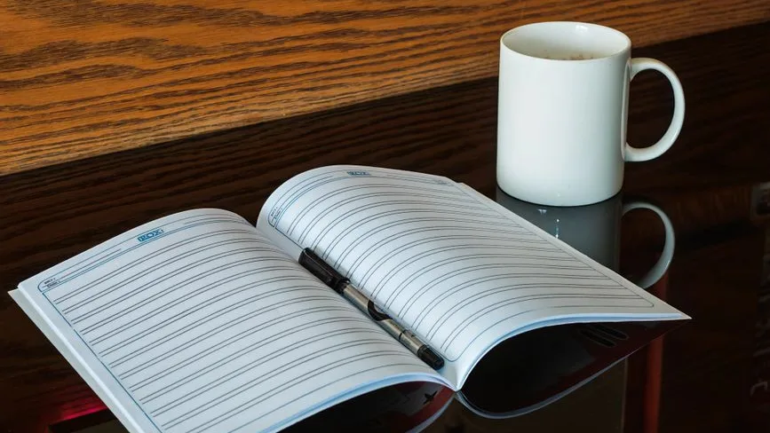 Un carnet ouvert, un stylo et une tasse de café sur une table